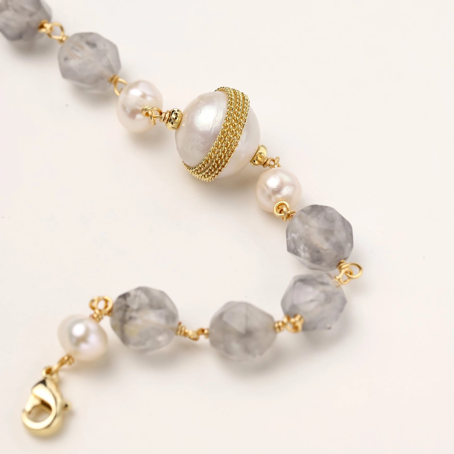 Gold-plated bracelet with white freshwater pearls and translucent grey crystals, featuring mesh-wrapped baroque pearl centerpiece