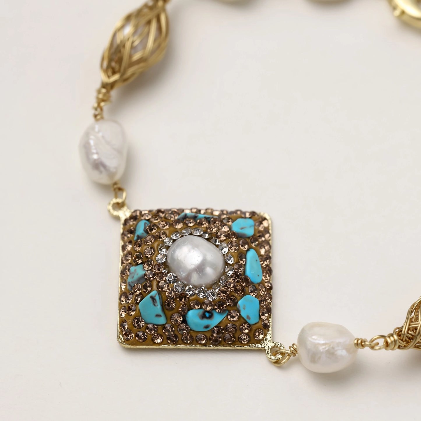 Ornate gold-plated bracelet with square turquoise and crystal centerpiece, freshwater pearls, and decorative chain links