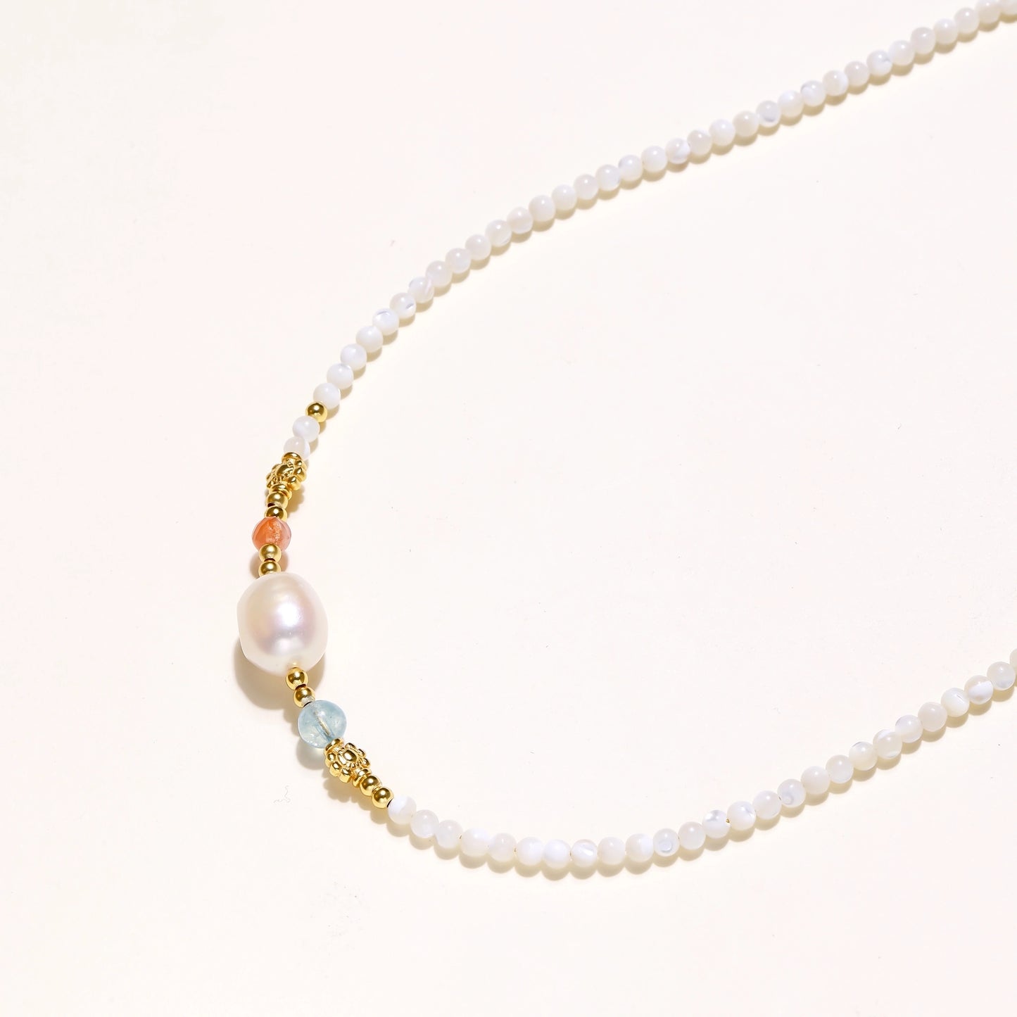 Delicate white beaded necklace with central freshwater pearl and gold-toned emerald accents on white background.