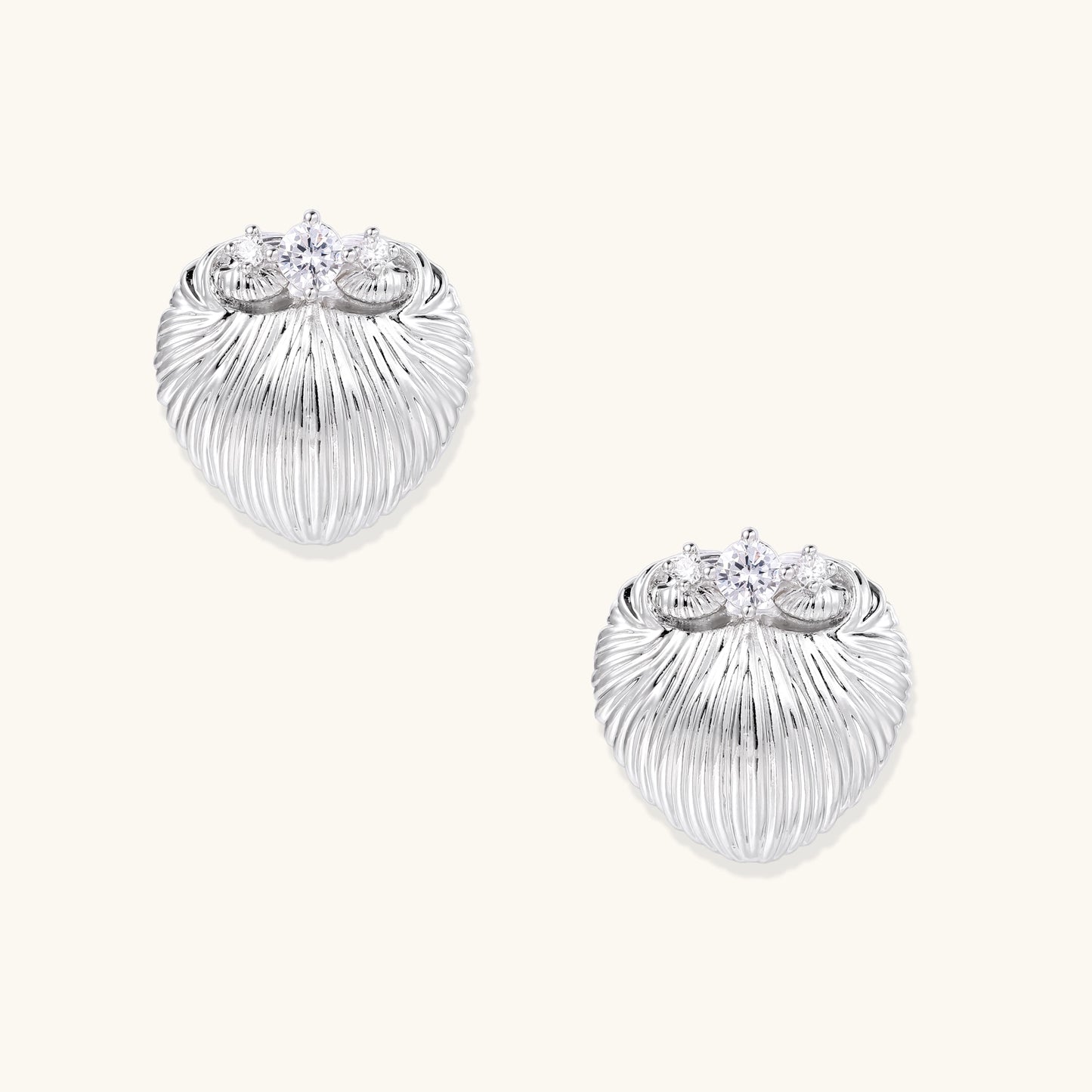 Pair of gold-plated heart-shaped earrings with vertical ribbed texture and sparkling zirconia stones at top on white background.