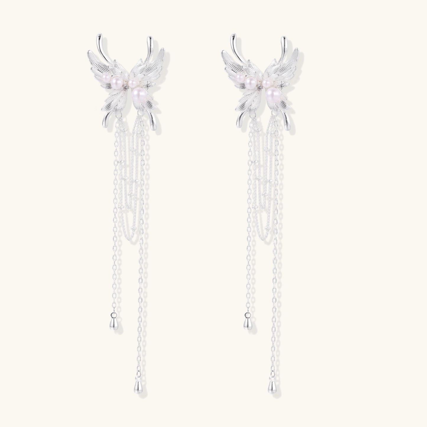 Elegant silver-plated drop earrings with wing-shaped tops, white pearl accents, and long chain tassels on white background.