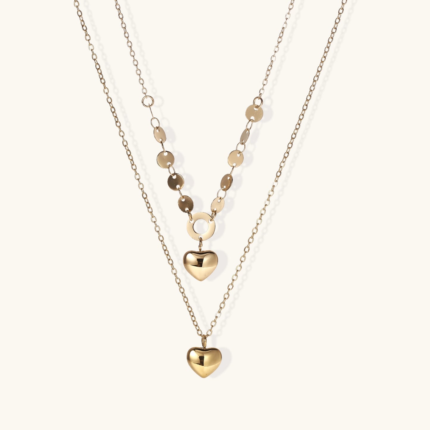 Three-layer gold-plated necklace set with disc chain and two heart pendants on neutral background