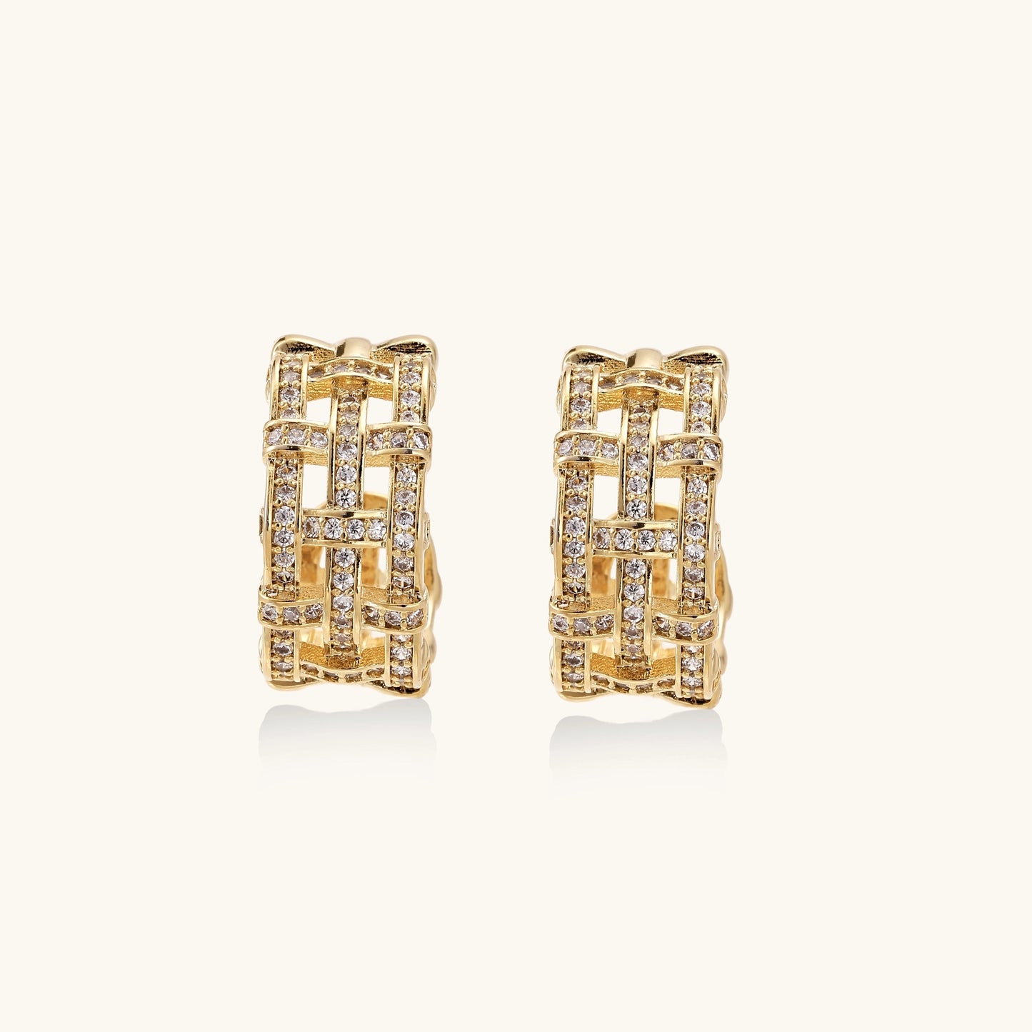 Close-up of geometric gold-plated hoop earrings with crystal pave in intricate lattice pattern on neutral background.