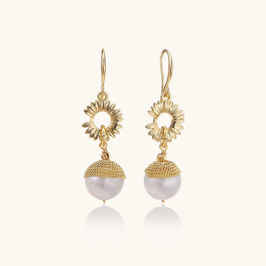 Gold-plated sunburst flower earrings with baroque pearl drops and textured metal caps on neutral background.