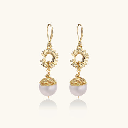 Gold-plated sunburst flower earrings with baroque pearl drops and textured metal caps on neutral background.