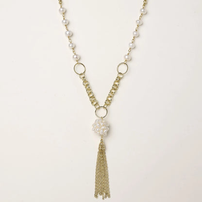 Layered gold-plated necklace with freshwater pearls, central pearl cluster, and chain tassel on cream background.