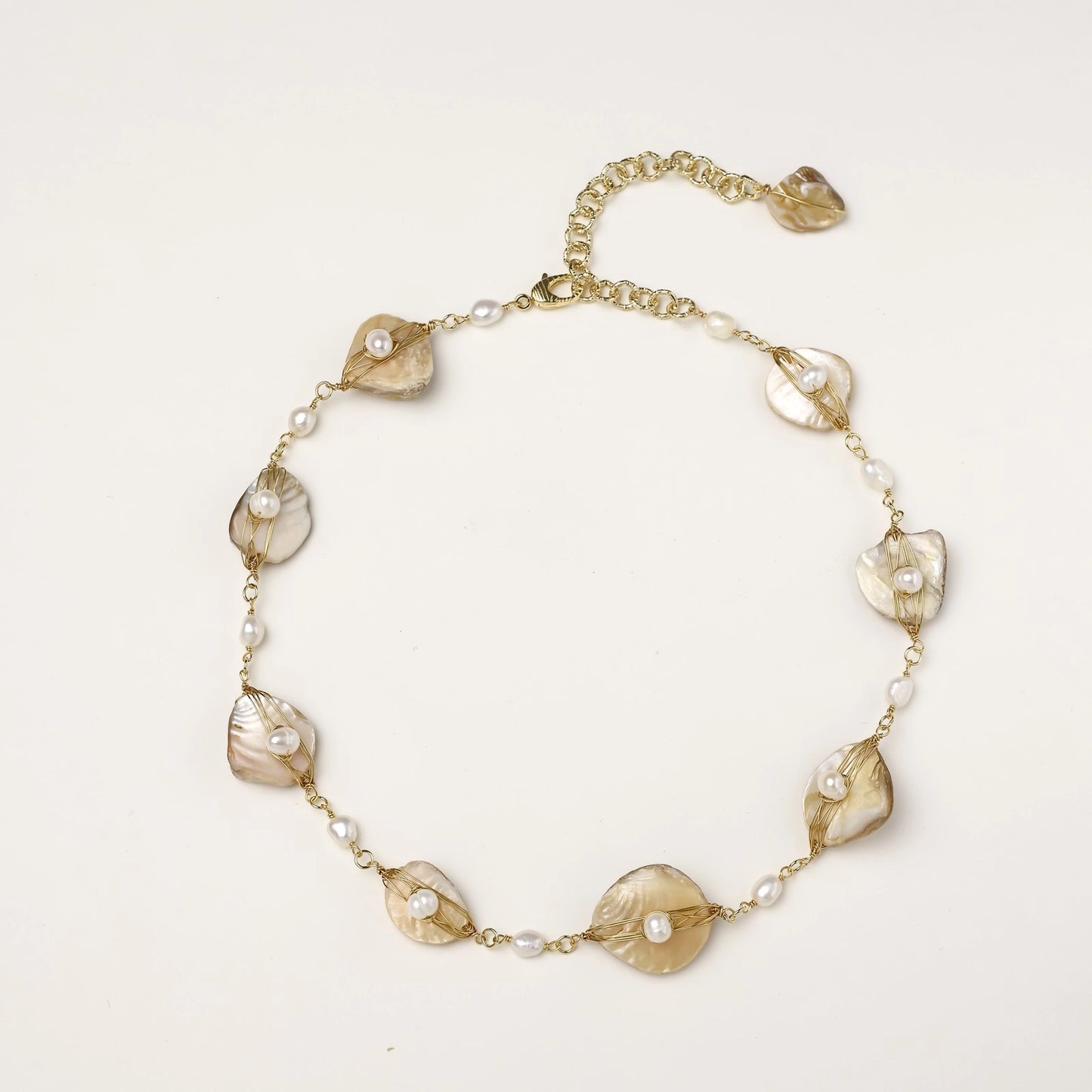 Delicate gold chain bracelet featuring iridescent shell charms with freshwater pearls on white background.