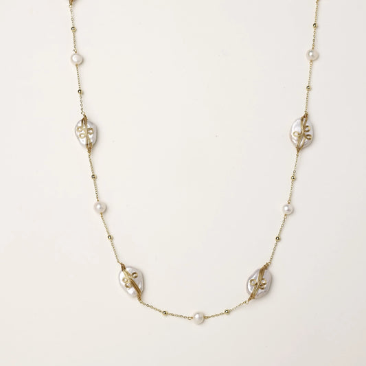 Delicate gold-plated necklace featuring translucent leaf-shaped baroque pearls and round freshwater pearls on neutral background.