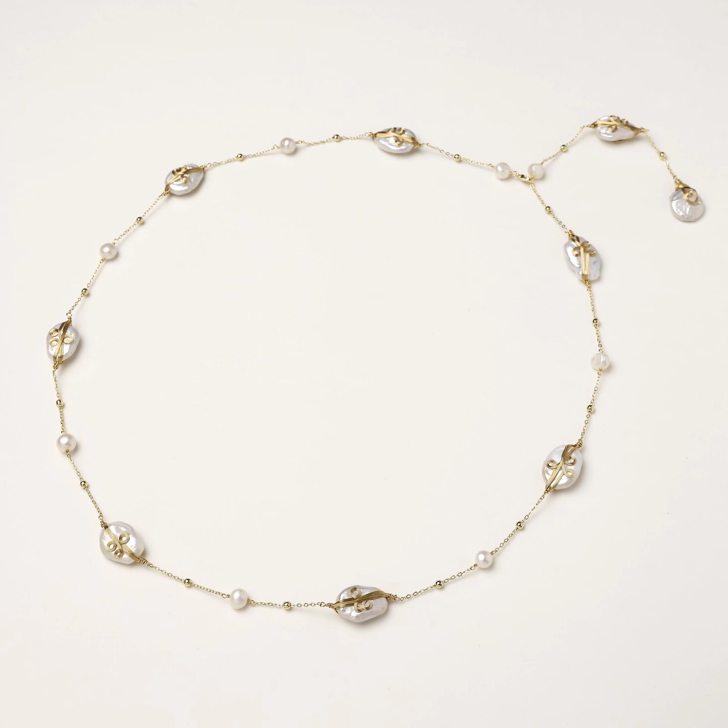 Delicate gold-plated necklace featuring translucent leaf-shaped baroque pearls and round freshwater pearls on neutral background.