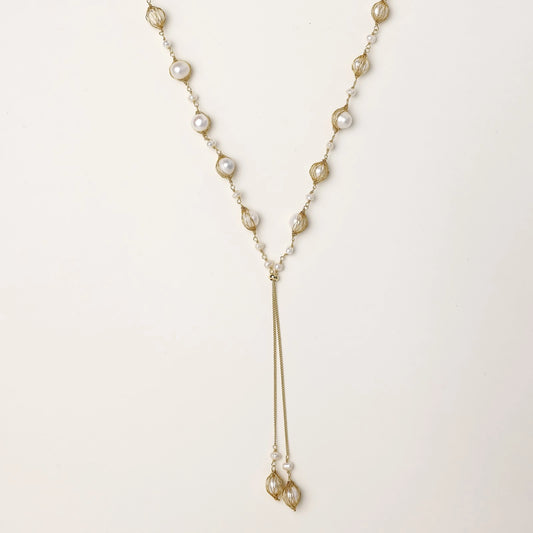 Long gold-plated lariat necklace with wire-wrapped freshwater pearls and chain tassel detail on cream background.