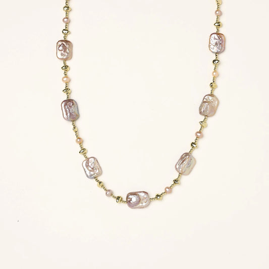 Long gold-plated necklace with iridescent baroque pearls and round freshwater pearls on cream background