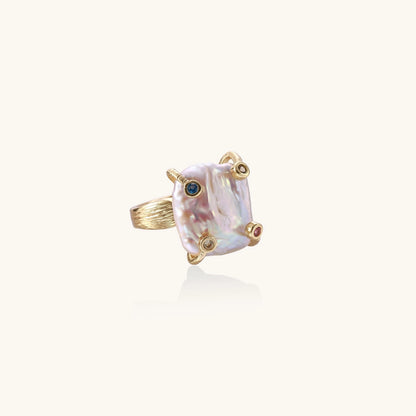 Gold-plated ring featuring large baroque freshwater pearl with small colorful gemstone accents on textured band