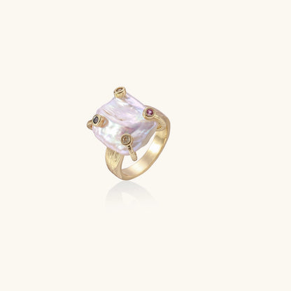 Gold-plated ring featuring large baroque freshwater pearl with small colorful gemstone accents on textured band