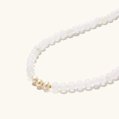 Stretch bracelet with white jade beads, freshwater pearls, and orange agate centerpiece on cream background.