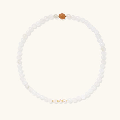 Stretch bracelet with white jade beads, freshwater pearls, and orange agate centerpiece on cream background.