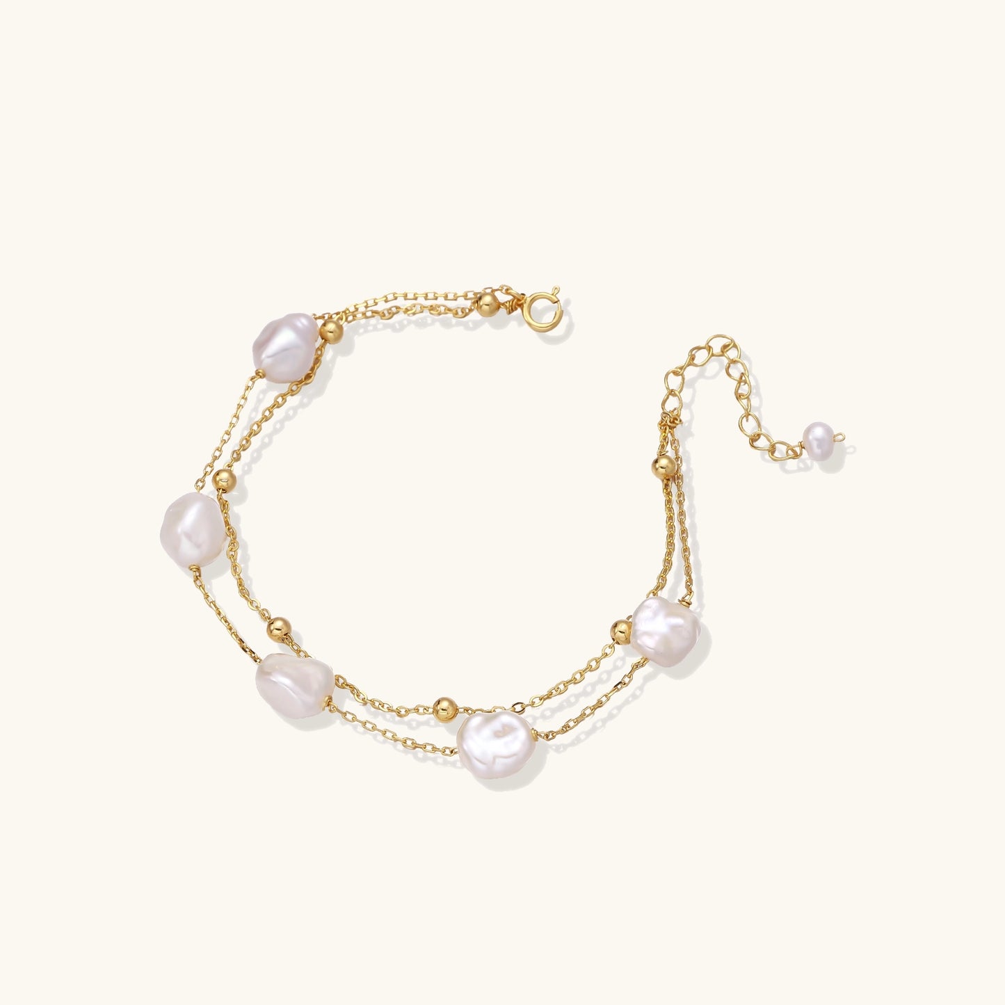 Delicate multi-layered gold-plated bracelet with irregular baroque pearls and freshwater pearls on cream background.