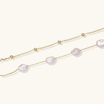 Delicate multi-layered gold-plated bracelet with irregular baroque pearls and freshwater pearls on cream background.