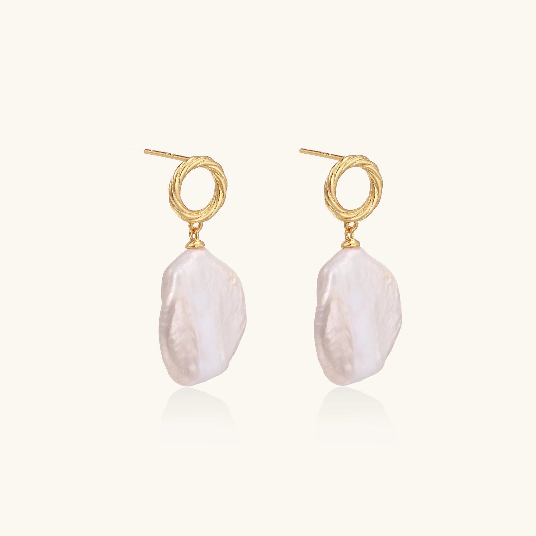 Gold-plated twisted stud earrings with large blush baroque pearls hanging elegantly on white background.