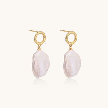 Gold-plated twisted stud earrings with large blush baroque pearls hanging elegantly on white background.