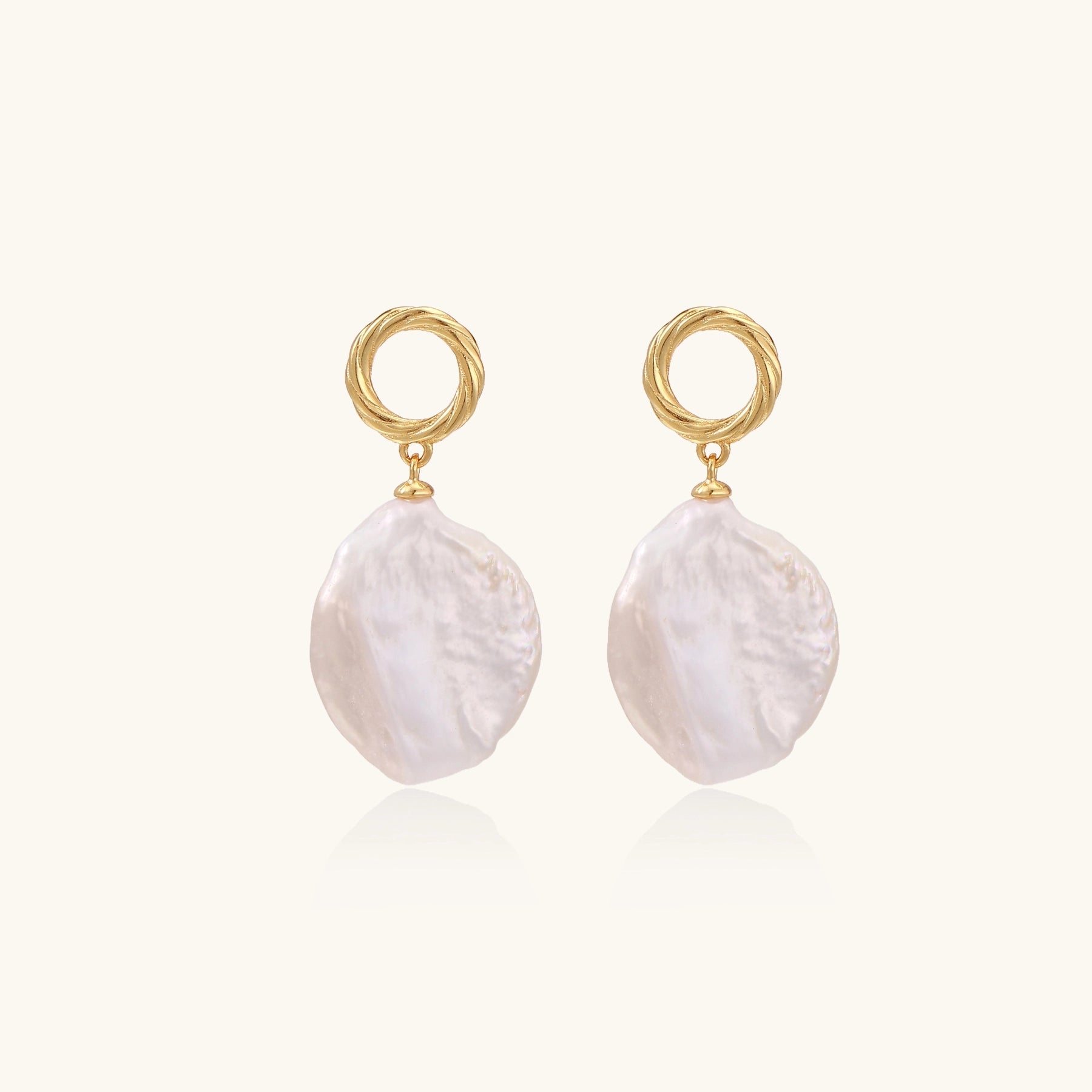 Gold-plated twisted stud earrings with large blush baroque pearls hanging elegantly on white background.
