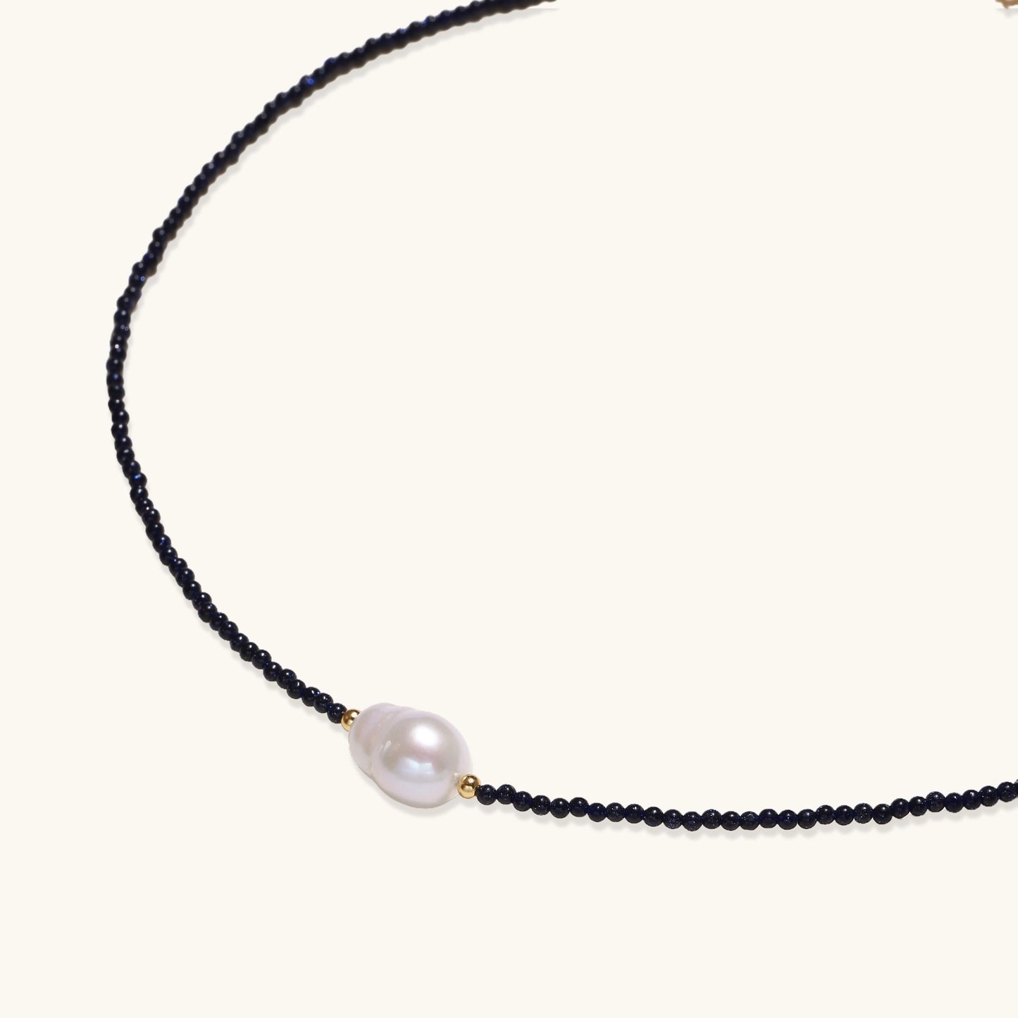 Elegant necklace with blue sandstone beads and baroque pearl centerpiece with gold accents on neutral background.