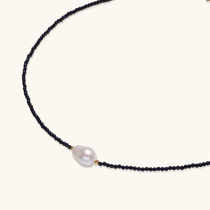 Elegant necklace with blue sandstone beads and baroque pearl centerpiece with gold accents on neutral background.