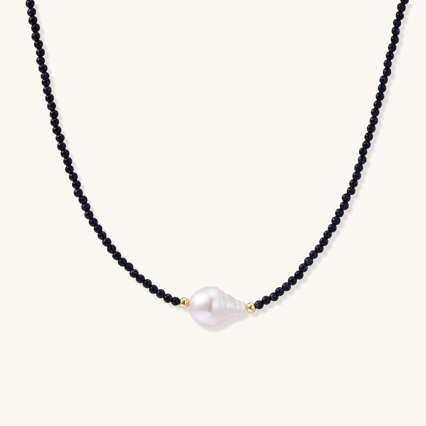 Elegant necklace with blue sandstone beads and baroque pearl centerpiece with gold accents on neutral background.