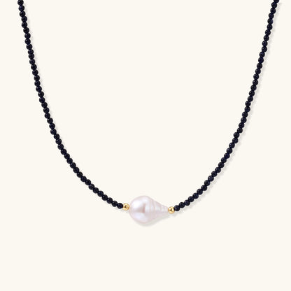 Elegant necklace with blue sandstone beads and baroque pearl centerpiece with gold accents on neutral background.