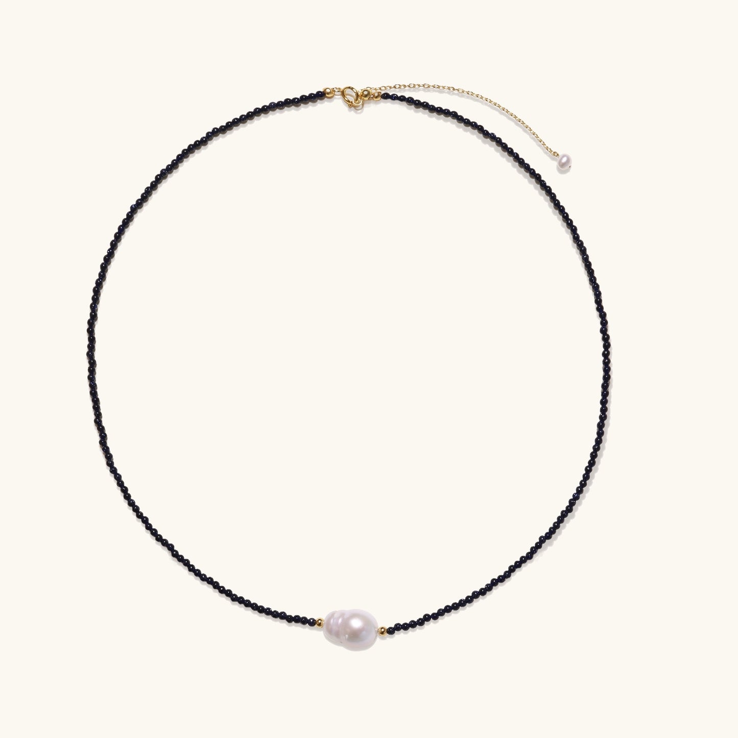 Elegant necklace with blue sandstone beads and baroque pearl centerpiece with gold accents on neutral background.