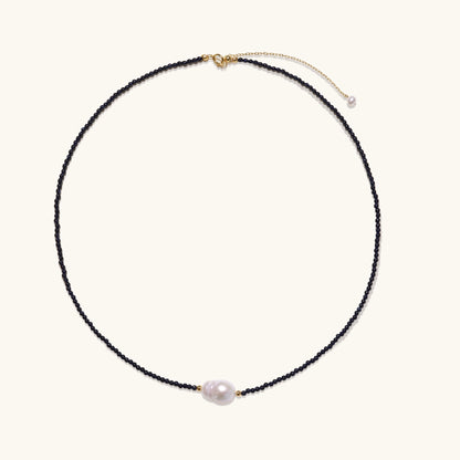 Elegant necklace with blue sandstone beads and baroque pearl centerpiece with gold accents on neutral background.