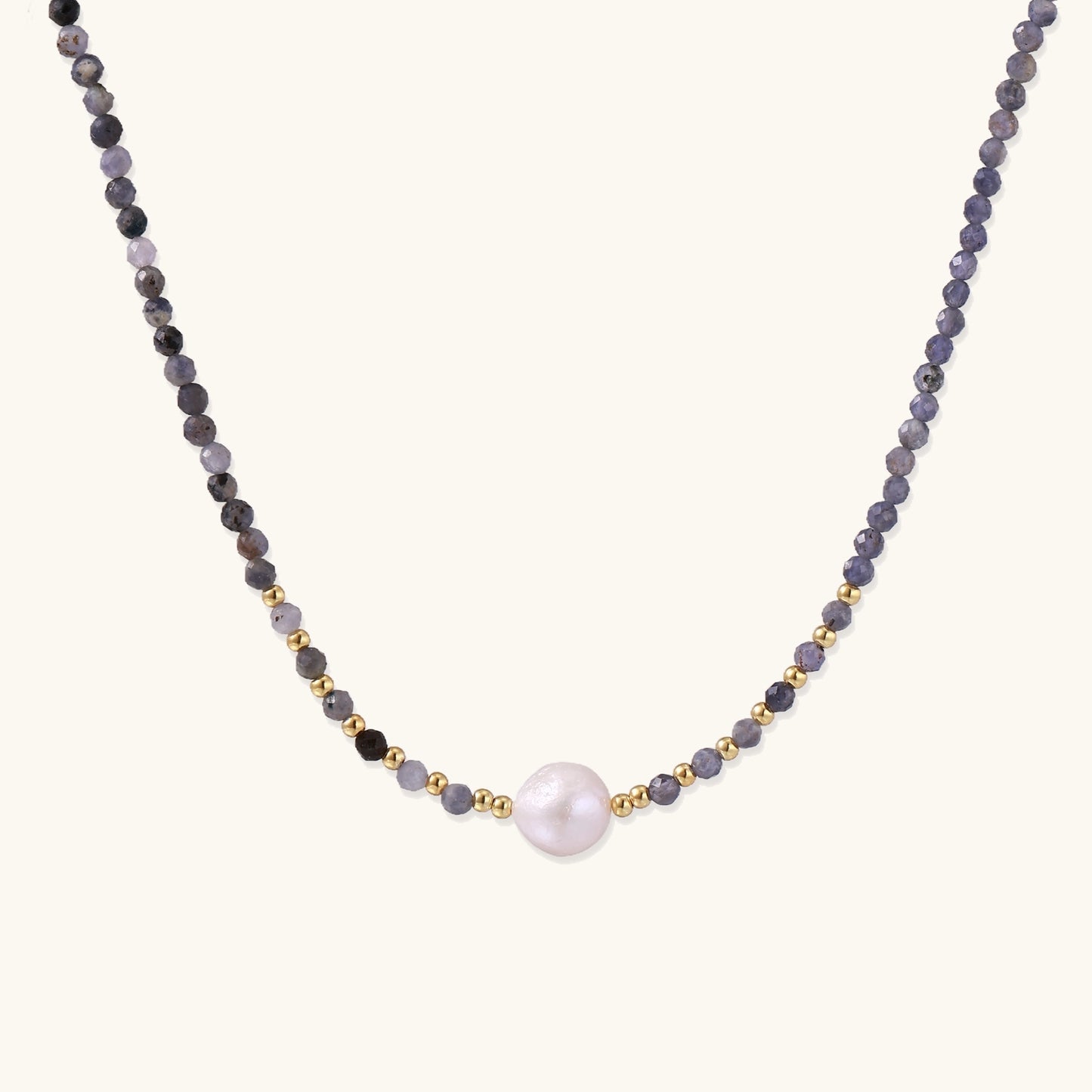 Delicate beaded necklace with violet iolite stones, gold spacers, and central white freshwater pearl on neutral background.