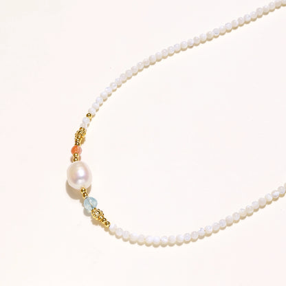 Delicate white beaded necklace with central freshwater pearl and gold-toned emerald accents on white background.