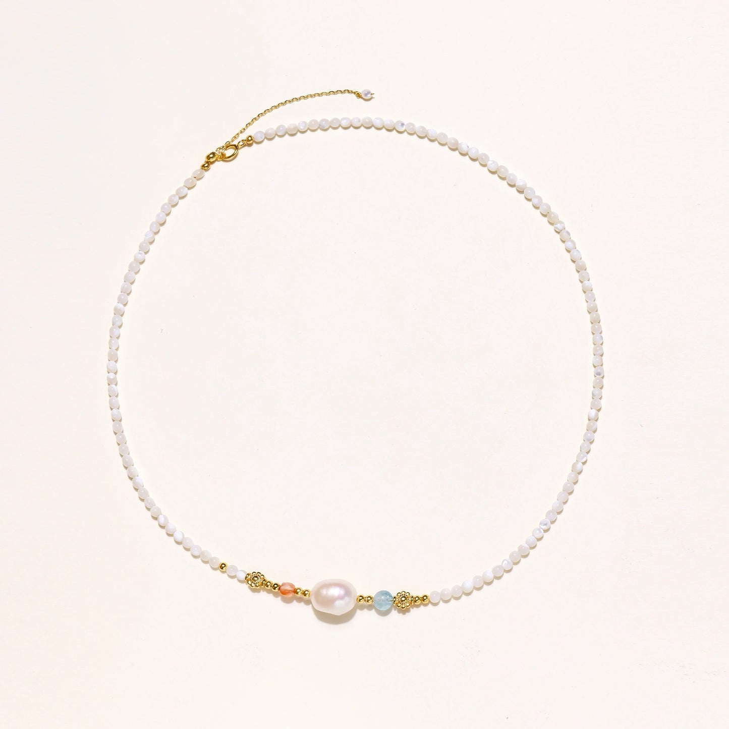 Delicate white beaded necklace with central freshwater pearl and gold-toned emerald accents on white background.