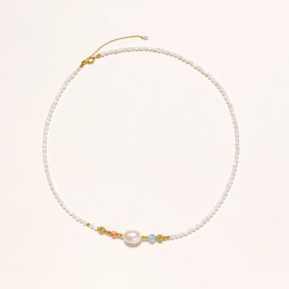Delicate white beaded necklace with central freshwater pearl and gold-toned emerald accents on white background.