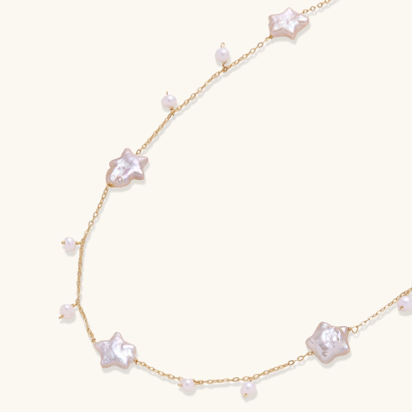 Delicate gold chain necklace with star-shaped baroque pearls and small freshwater pearls on cream background.