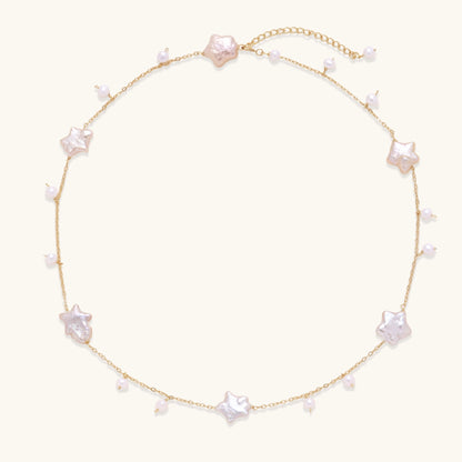 Delicate gold chain necklace with star-shaped baroque pearls and small freshwater pearls on cream background.