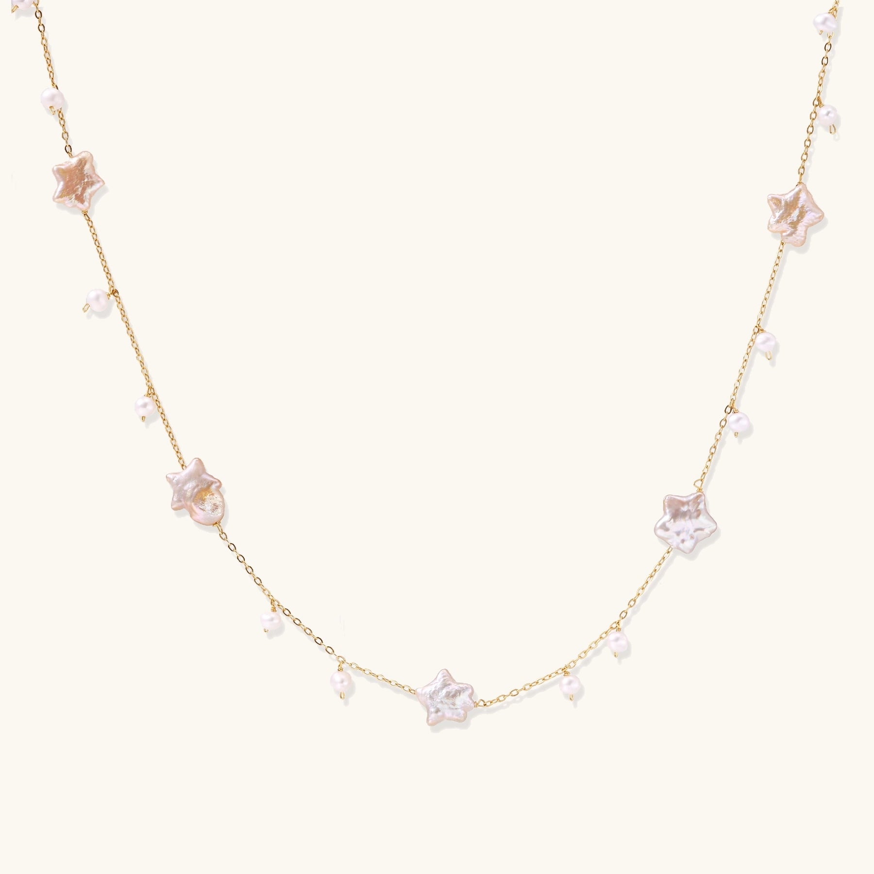 Delicate gold chain necklace with star-shaped baroque pearls and small freshwater pearls on cream background.