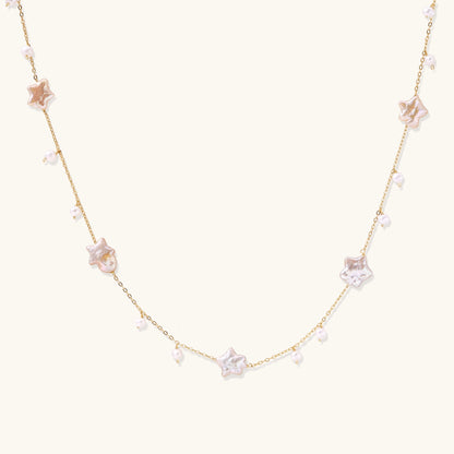 Delicate gold chain necklace with star-shaped baroque pearls and small freshwater pearls on cream background.