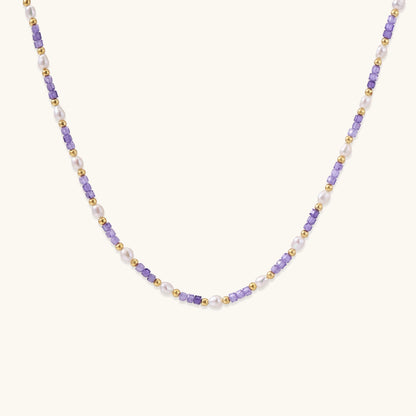 Delicate beaded necklace with alternating purple zirconia stones, white freshwater pearls, and gold-plated spacers on cream background.