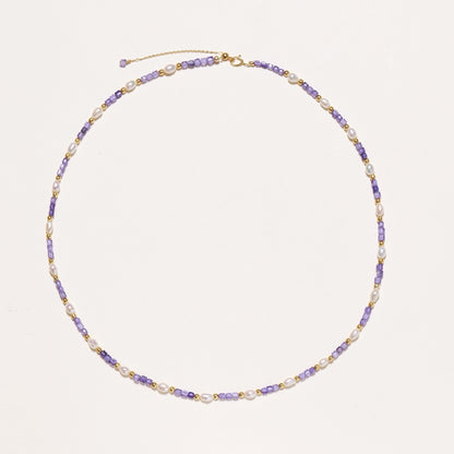 Delicate beaded necklace with alternating purple zirconia stones, white freshwater pearls, and gold-plated spacers on cream background.