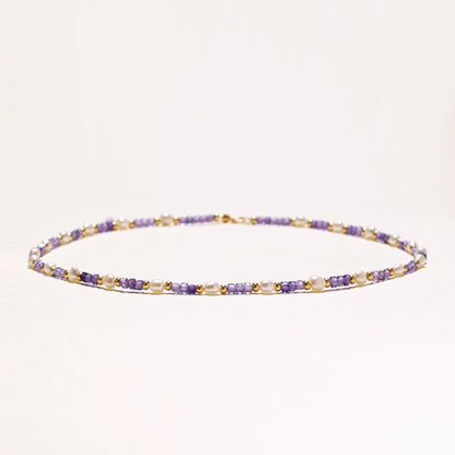 Delicate beaded necklace with alternating purple zirconia stones, white freshwater pearls, and gold-plated spacers on cream background.