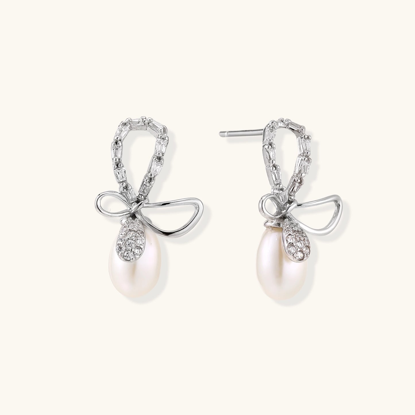 Sterling silver stud earrings with baguette crystal bow design and freshwater pearl drops on white background