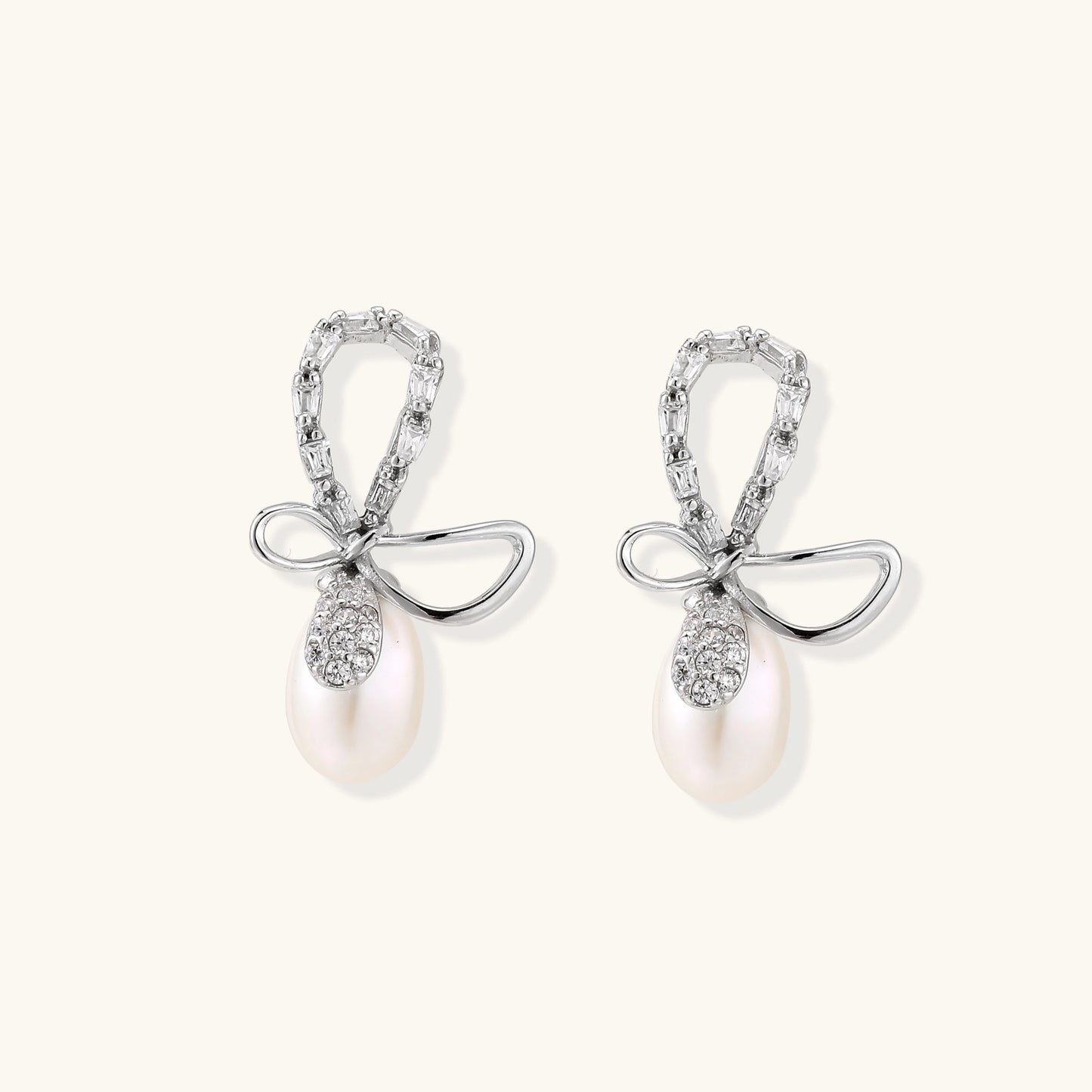 Sterling silver stud earrings with baguette crystal bow design and freshwater pearl drops on white background