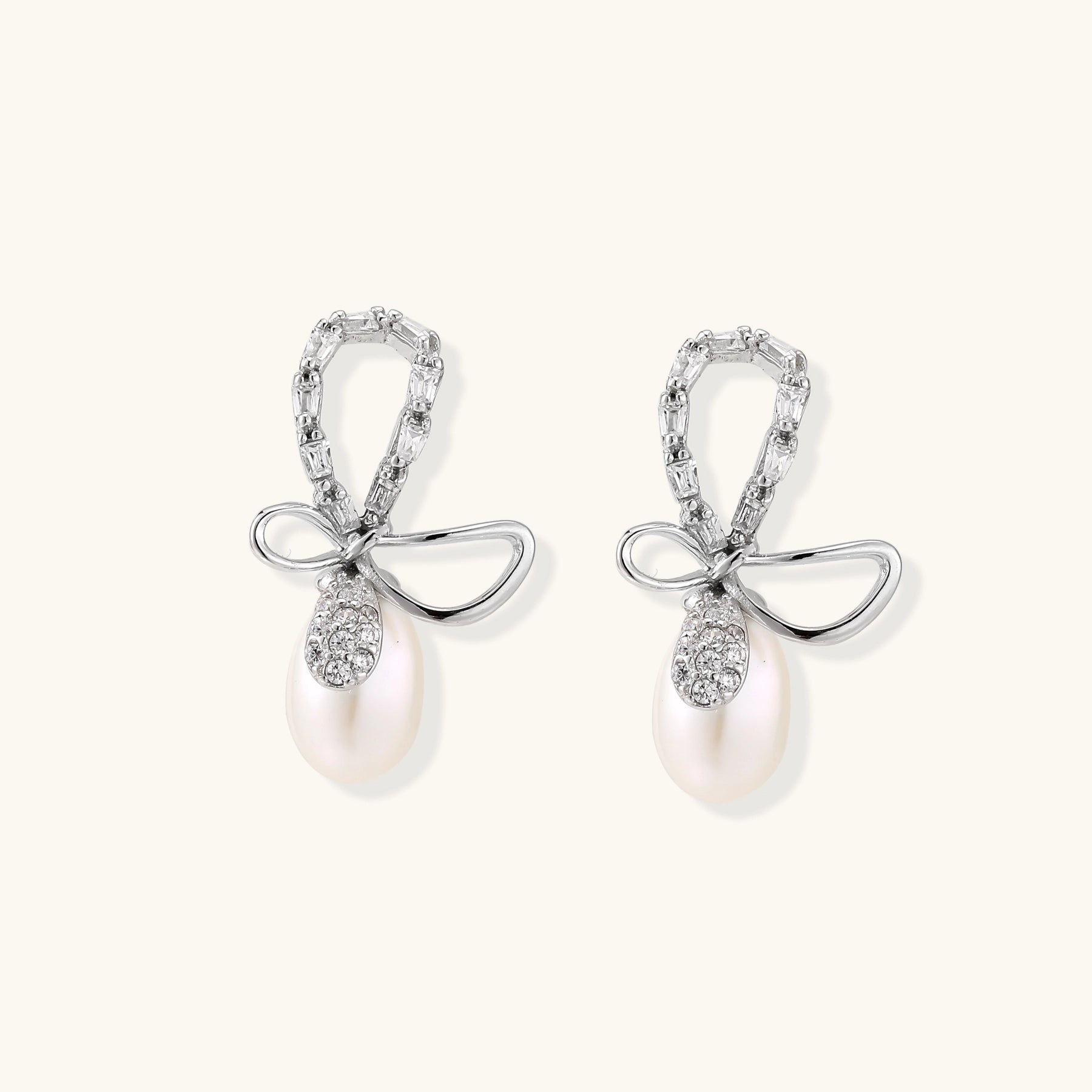 Sterling silver stud earrings with baguette crystal bow design and freshwater pearl drops on white background