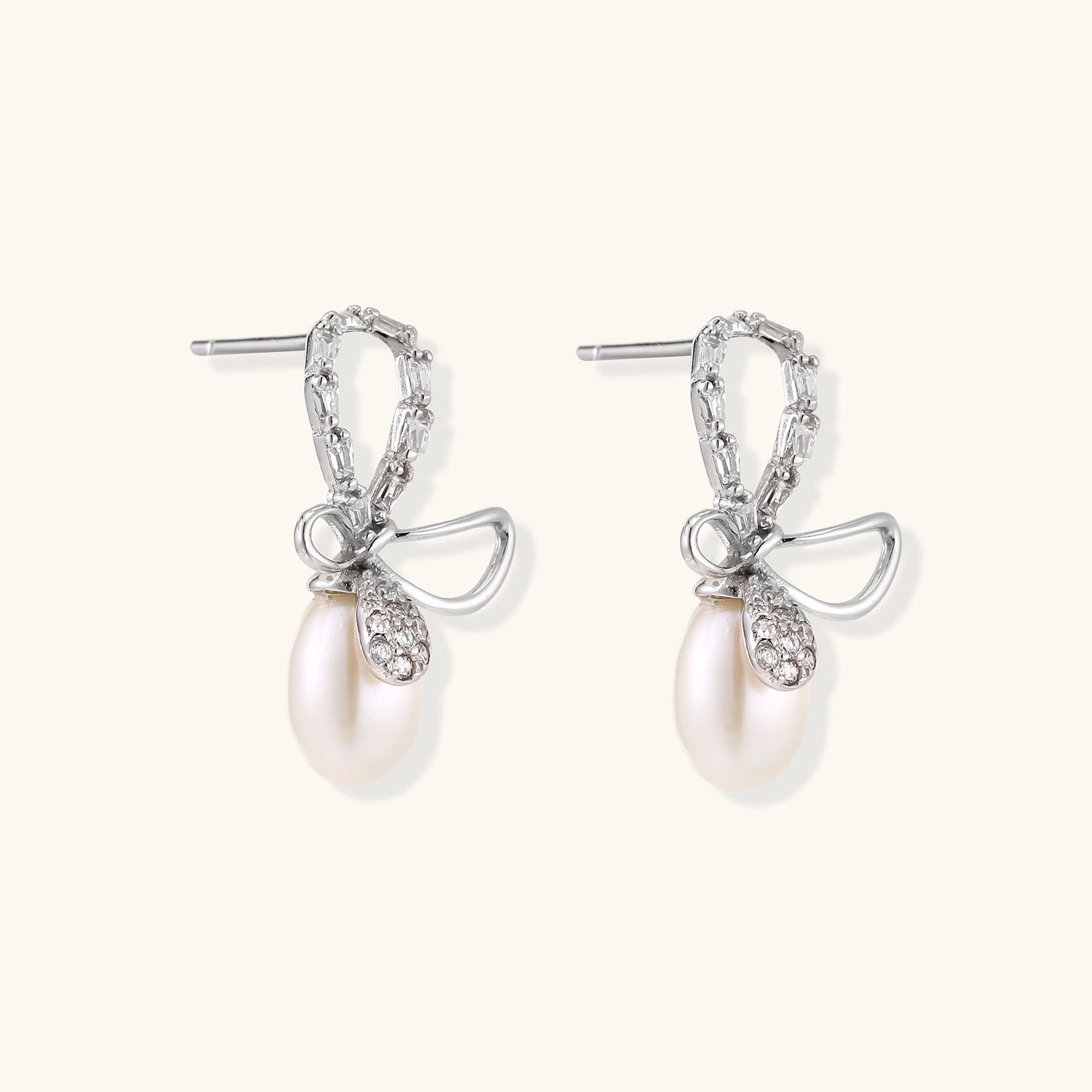 Sterling silver stud earrings with baguette crystal bow design and freshwater pearl drops on white background