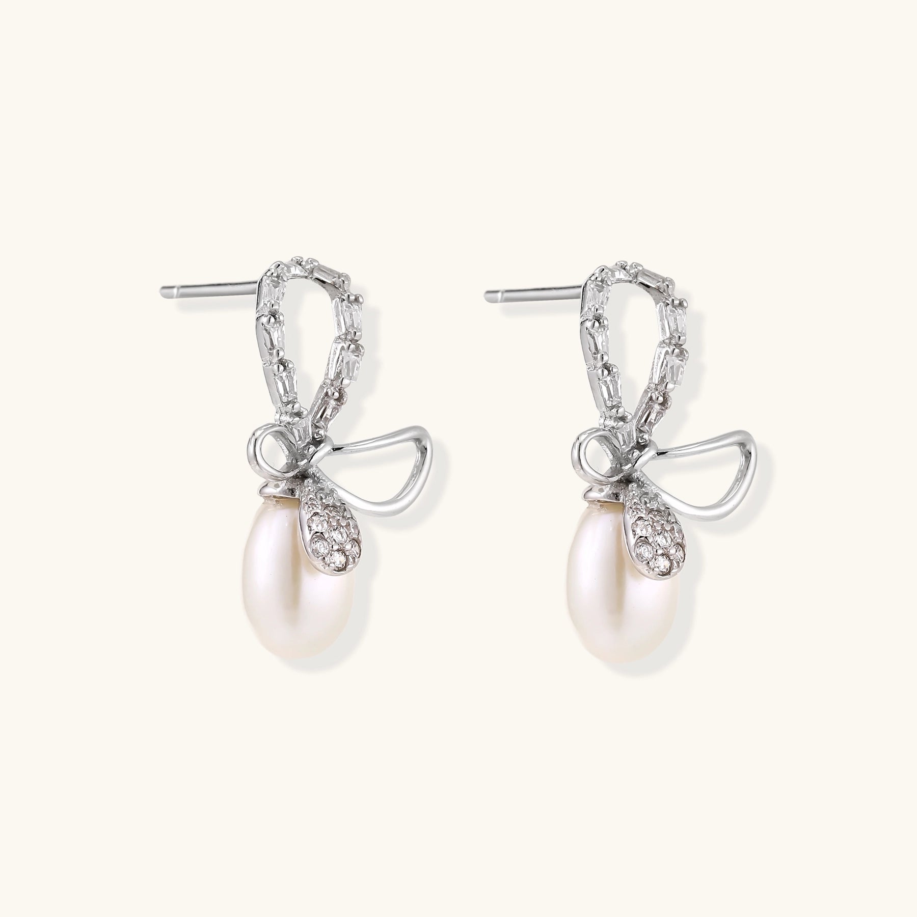 Sterling silver stud earrings with baguette crystal bow design and freshwater pearl drops on white background