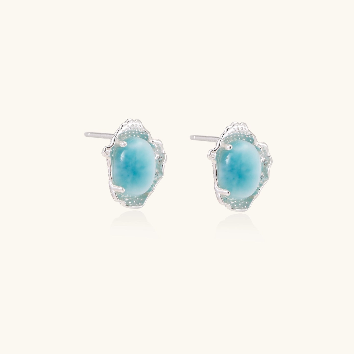 Close-up of sterling silver stud earrings with oval larimar stones in flowing wave-like settings on white background.