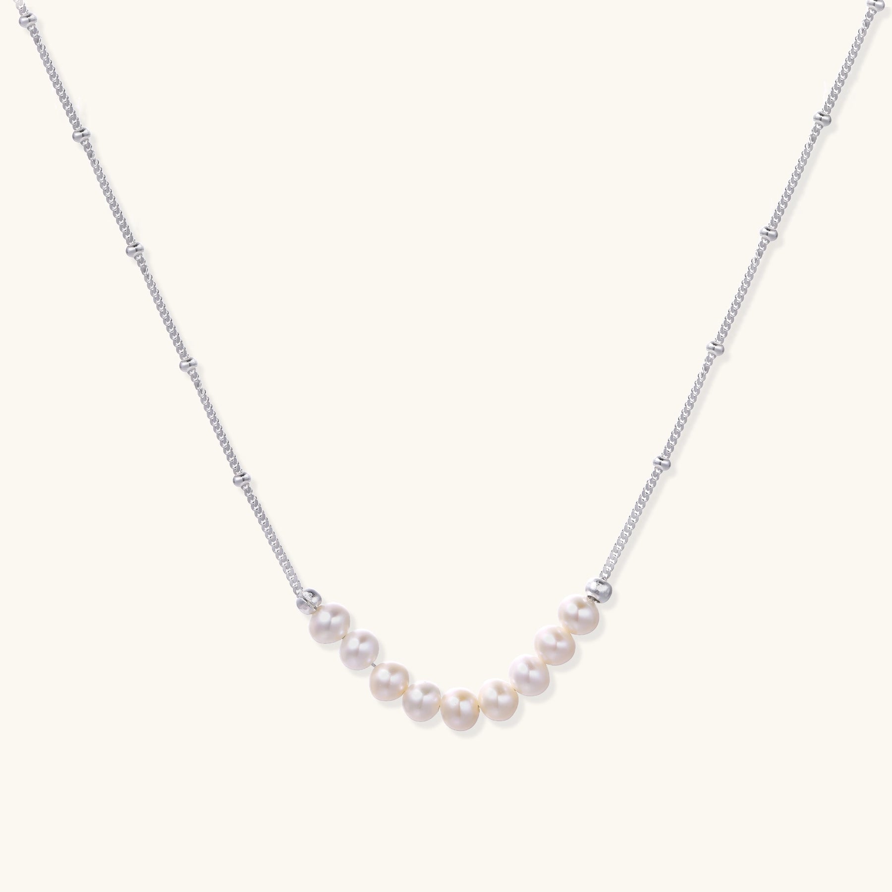 Delicate sterling silver chain with small white freshwater pearls arranged asymmetrically on white background.