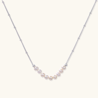 Delicate sterling silver chain with small white freshwater pearls arranged asymmetrically on white background.