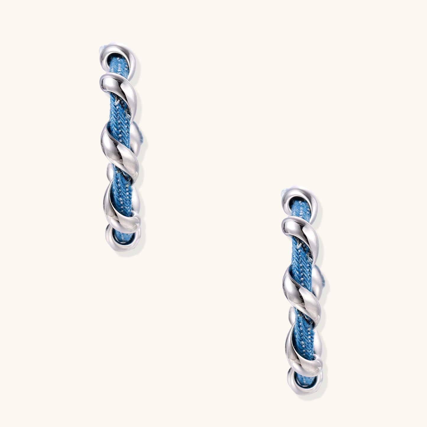 Twisted hoop earrings featuring blue denim fabric braided with gold-plated metal in a spiral design on white background.